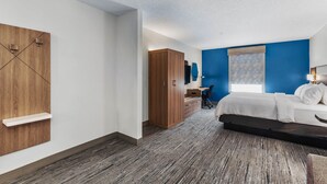 A bedroom with a bed, a desk, a wardrobe, and a window with blinds.