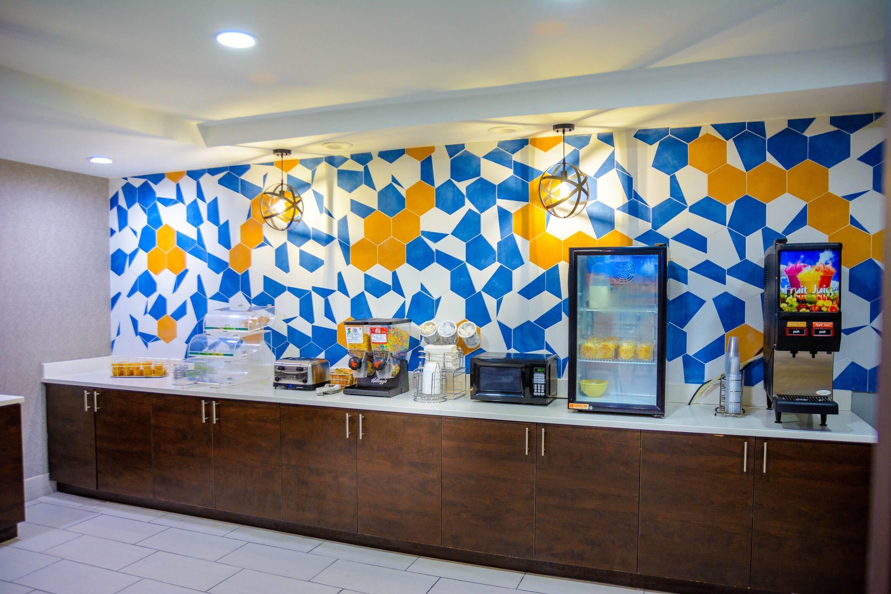 A breakfast bar with a geometric tile backsplash, a coffee machine, a microwave, and a juice dispenser.