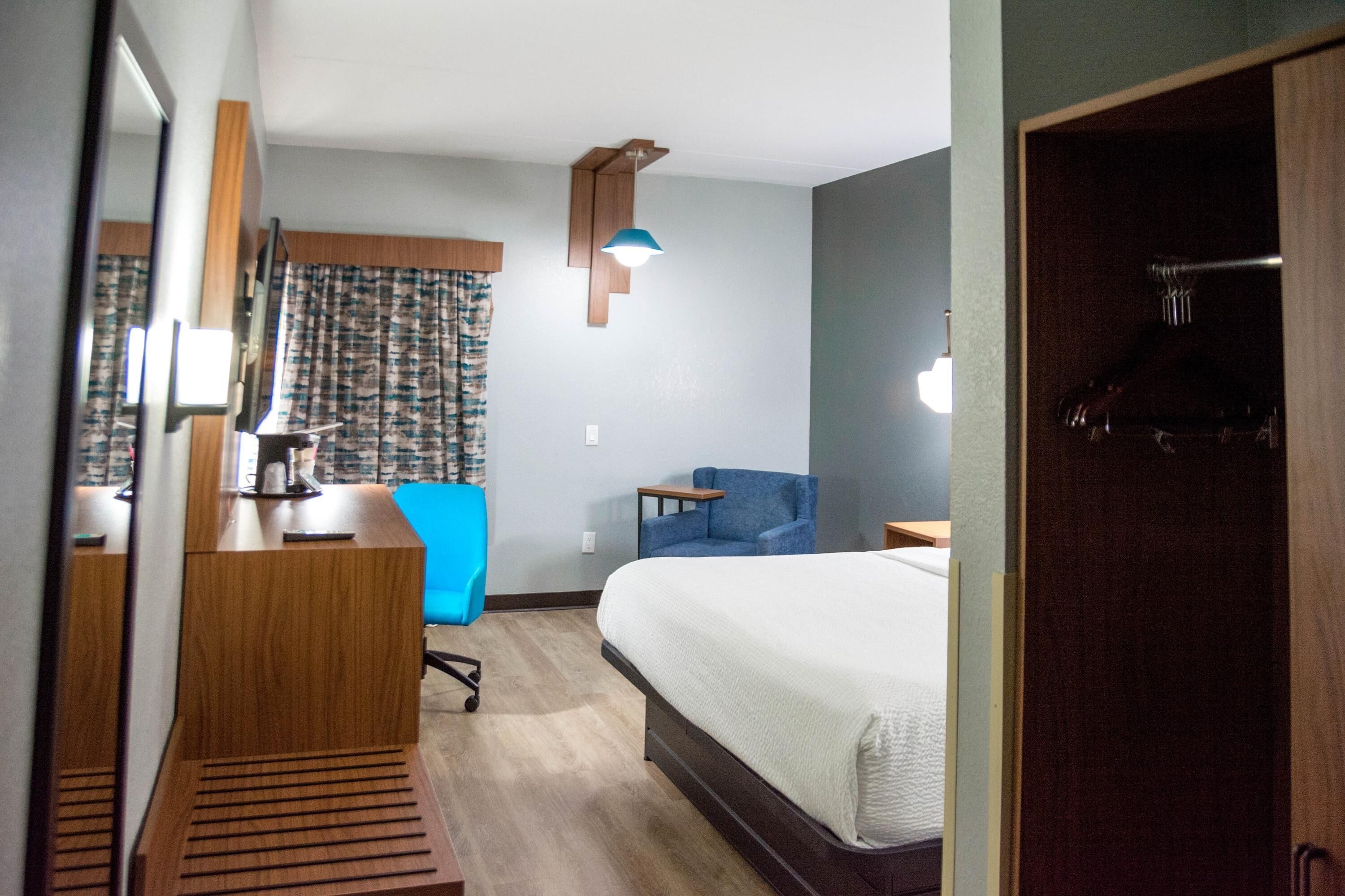 A hotel room with a bed, a desk, a chair, and a wardrobe.