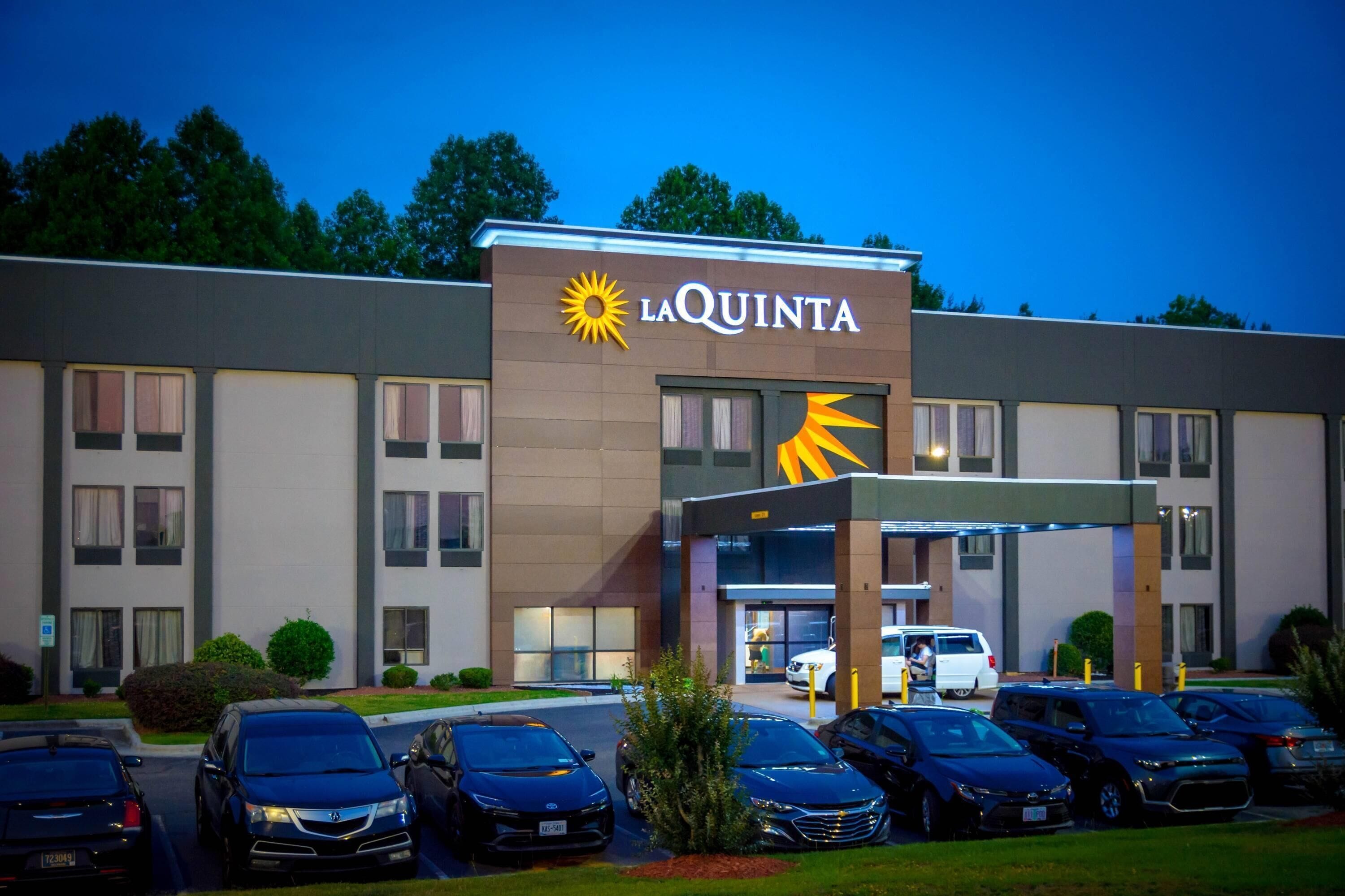 A La Quinta hotel with a modern facade, a parking lot, and a clear sky.