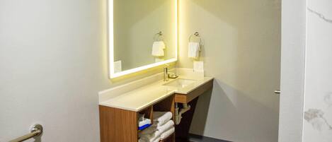 A bathroom with a wooden vanity, a large mirror with under-cabinet lighting, and a towel rack.