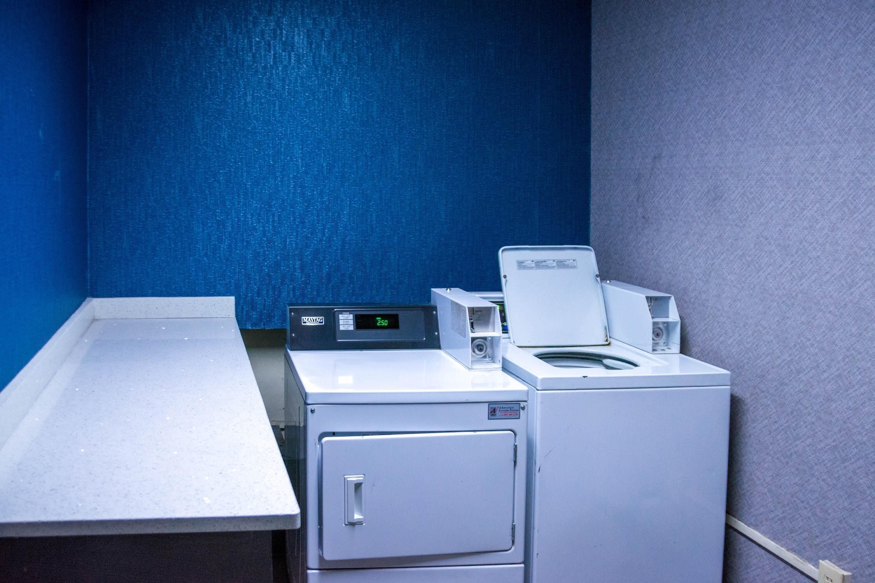 Un área de lavandería con lavadora y secadora, una mesa de metal y una pared azul.
