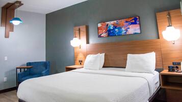 Habitación de hotel con una cama grande, un sillón azul, un cabecero de madera, un cuadro en la pared y dos lámparas de noche.