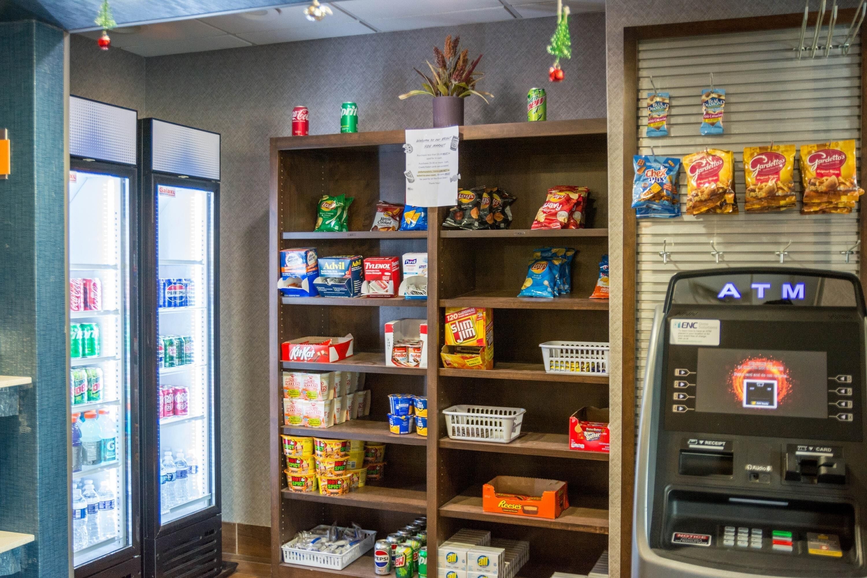 A convenience store with shelves stocked with snacks, beverages, and a refrigerated section. An ATM is visible on the right.