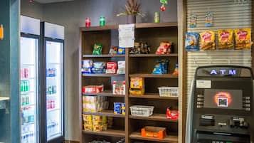 A convenience store with shelves stocked with snacks, beverages, and a refrigerated section. An ATM is visible on the right.