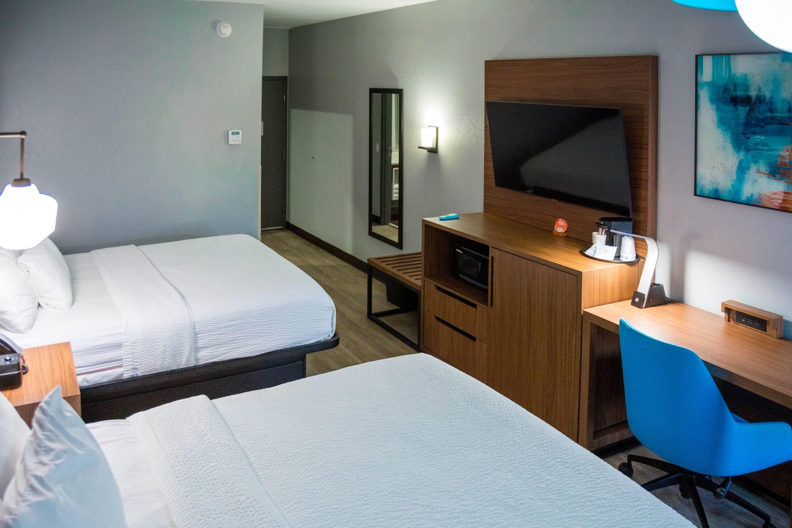 Habitación de hotel con dos camas, un escritorio, un televisor y un espejo.