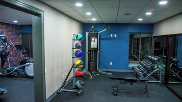 Un gimnasio con equipo de ejercicio, un soporte de balón medicinal en la pared y un espejo.