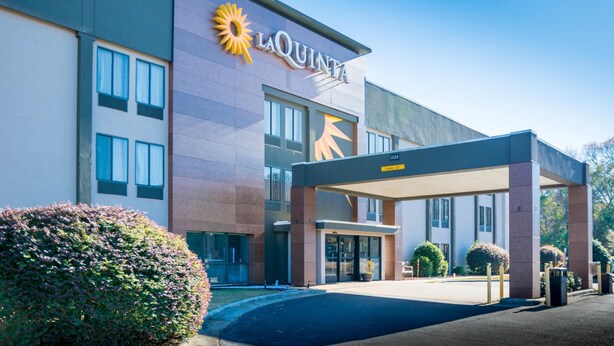 A modern hotel with a prominent 'La Quinta' sign, a covered entrance, and a landscaped area with bushes. - La Quinta Inn & Suites by Wyndham Fayetteville I-95 (Fayetteville)