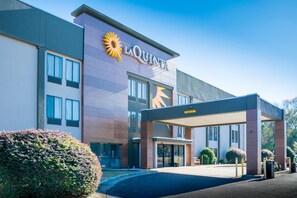 A modern hotel with a prominent 'La Quinta' sign, a covered entrance, and a landscaped area with bushes.