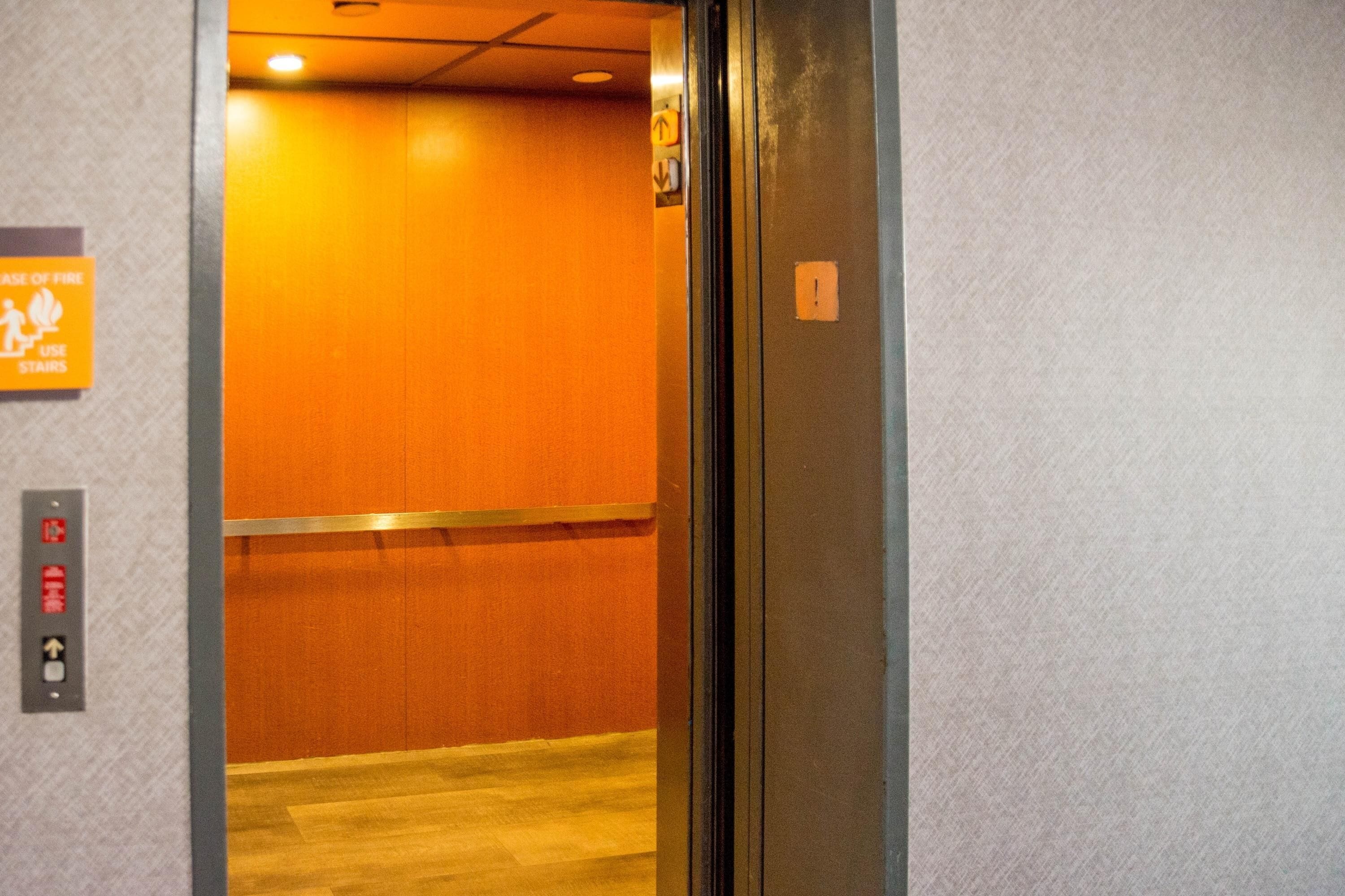 An elevator interior with orange walls and a wooden floor.
