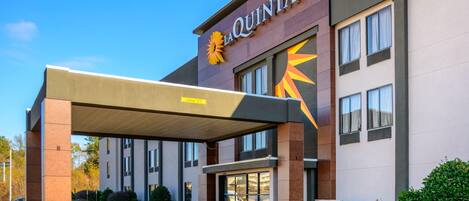 Hotel La Quinta con entrada cubierta, ventanas amplias y estacionamiento.