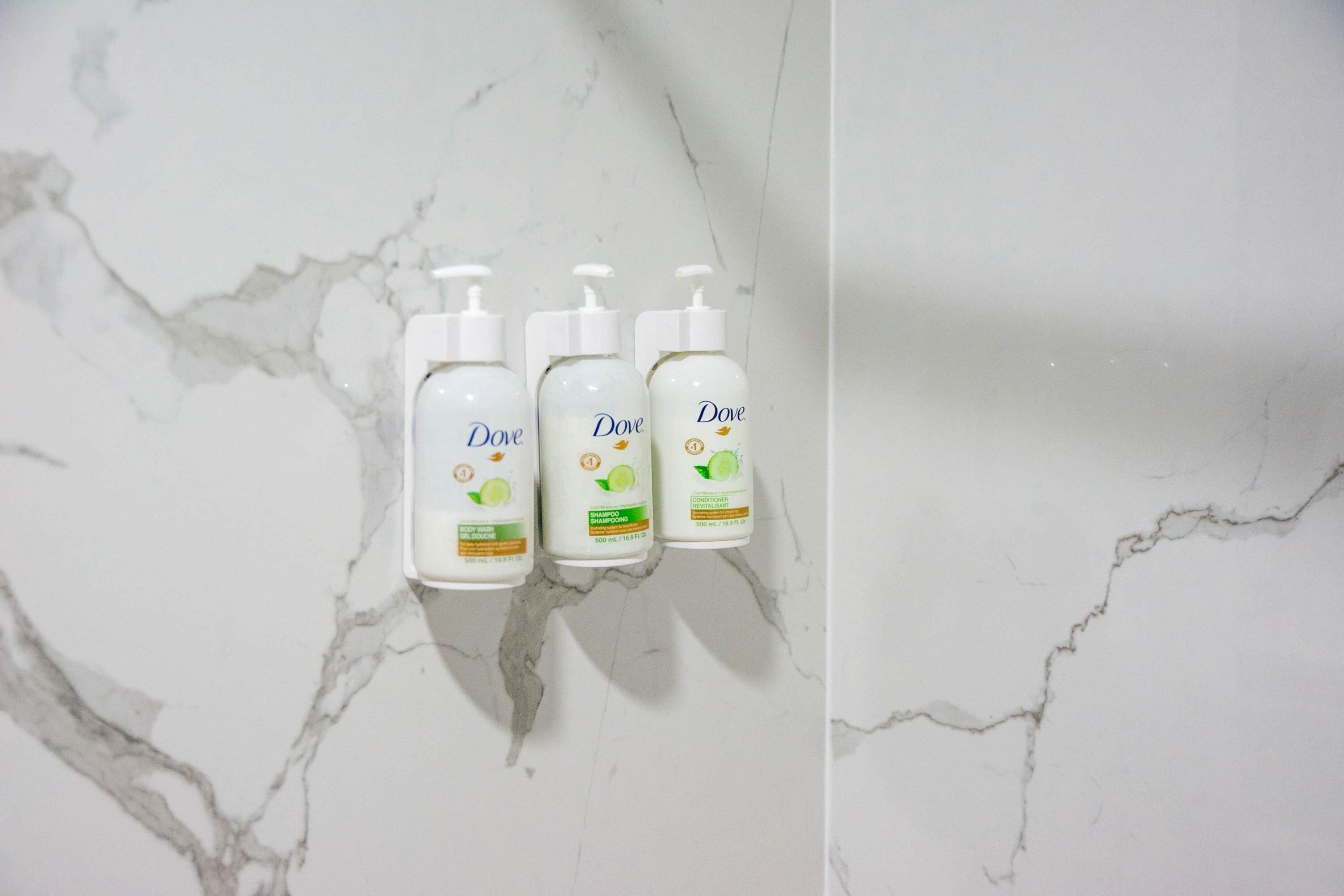 Trois bouteilles de shampoing Dove sur une surface en marbre.