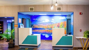 A reception area with a large mural, two reception desks, and potted plants. - La Quinta Inn & Suites by Wyndham Fayetteville I-95 (Fayetteville)
