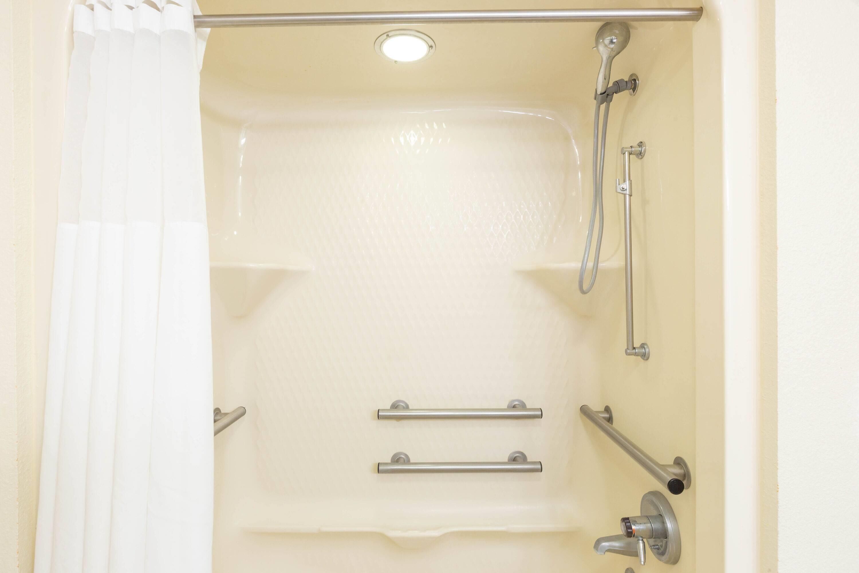 A bathroom with a bathtub, shower, and grab bars.