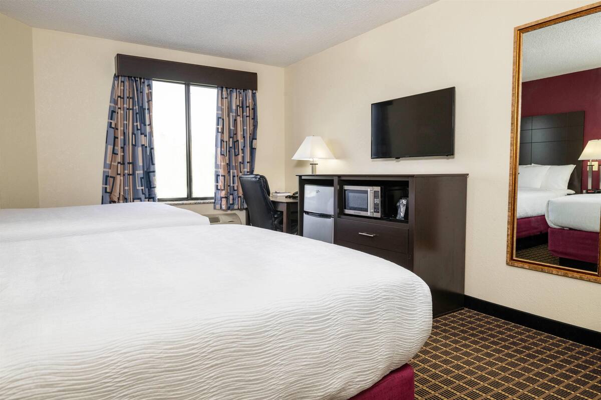 A hotel room with a large bed, a desk with a chair, a television, a microwave, and a mirror.