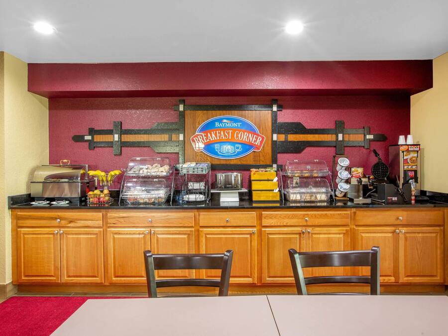 Ein Frühstücksbereich mit einem Schild, das 'Baymont Breakfast Corner' zeigt, ausgestattet mit verschiedenen Speisen und Geräten.
