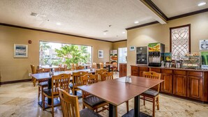 A dining area with wooden tables and chairs, a kitchen counter with appliances, and framed pictures on the walls. - Quality Inn & Suites Seabrook - NASA - Kemah (Seabrook)