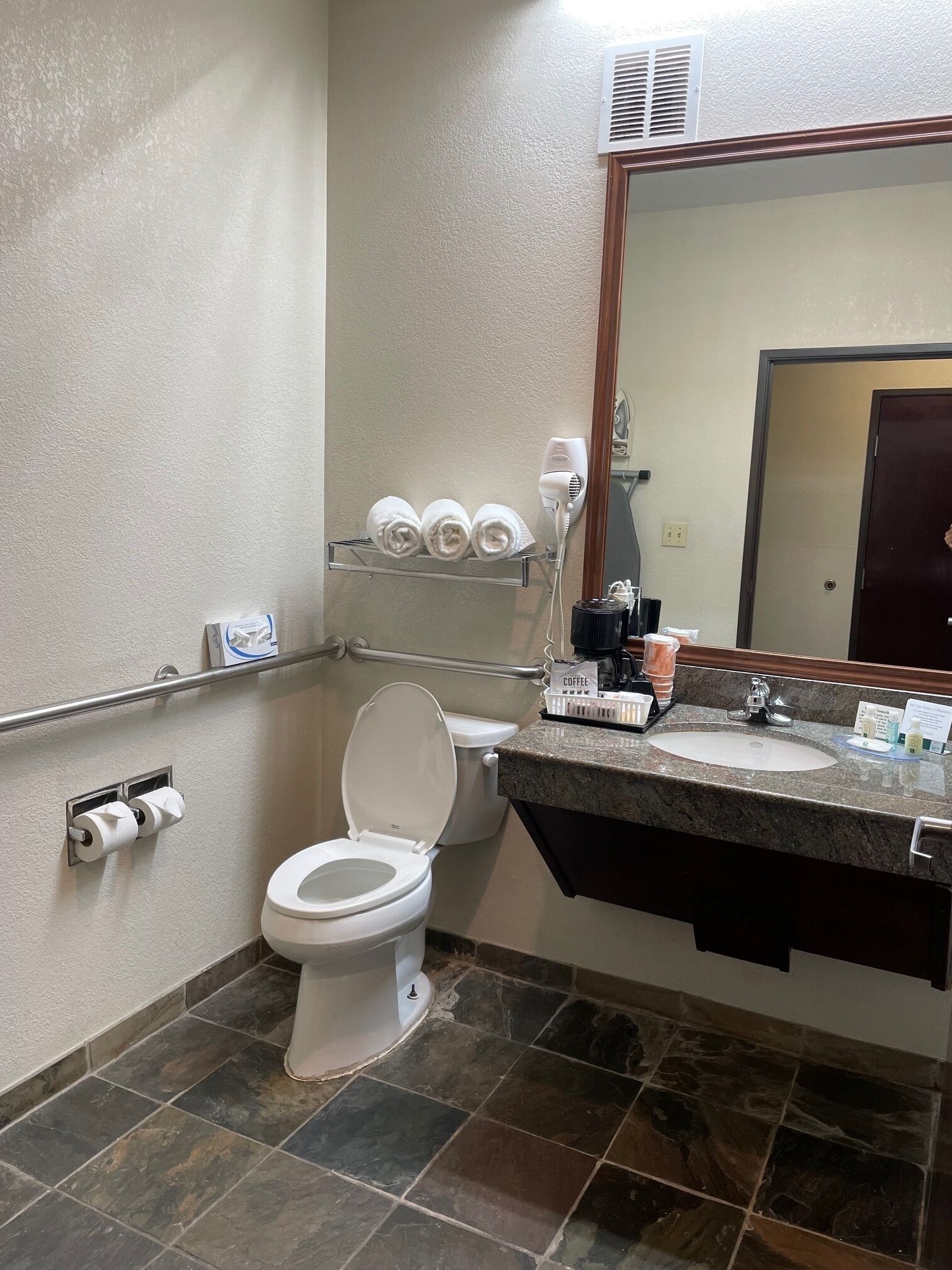 Een badkamer met een wit toilet, een wastafel met een marmeren aanrecht, een spiegel en een handdoekrek met handdoeken.