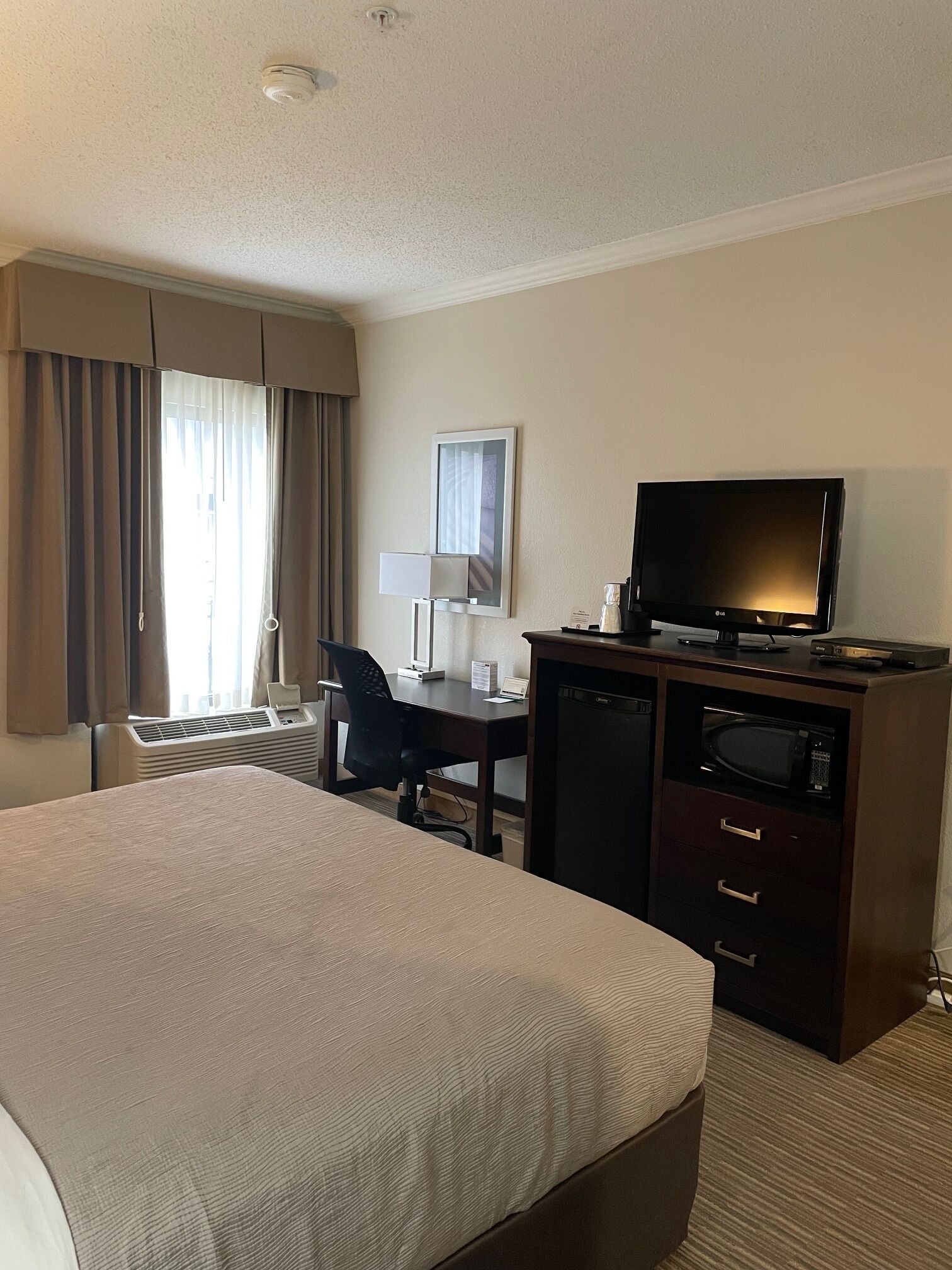 Una habitación de hotel con una cama, un escritorio con computadora, televisor y microondas.