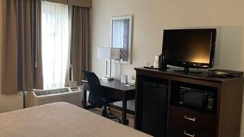 Una habitación de hotel con una cama, un escritorio con computadora, televisor y microondas.