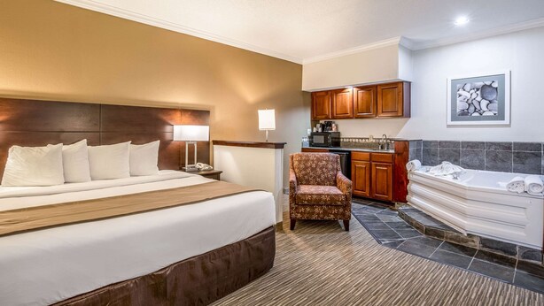 A hotel room with a large bed, a sitting area with a chair, a kitchenette, and a separate bathroom with a bathtub. - Quality Inn & Suites Seabrook - NASA - Kemah (Seabrook)
