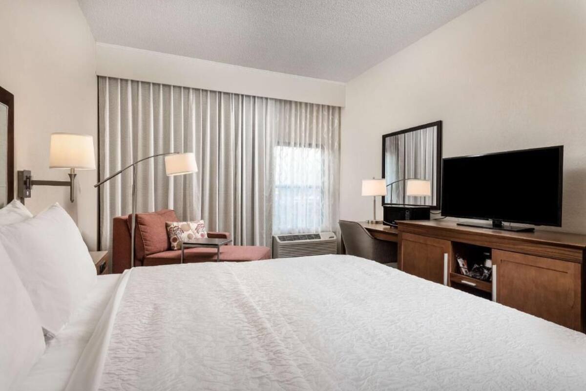 A hotel room with a large bed, a desk, a television, and a chair.