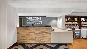Una zona d'entrada amb un cartell que diu 'Welcome to the Sun State', un taulell de recepció de fusta, un minibar i una exposició de serveis de l'hotel.