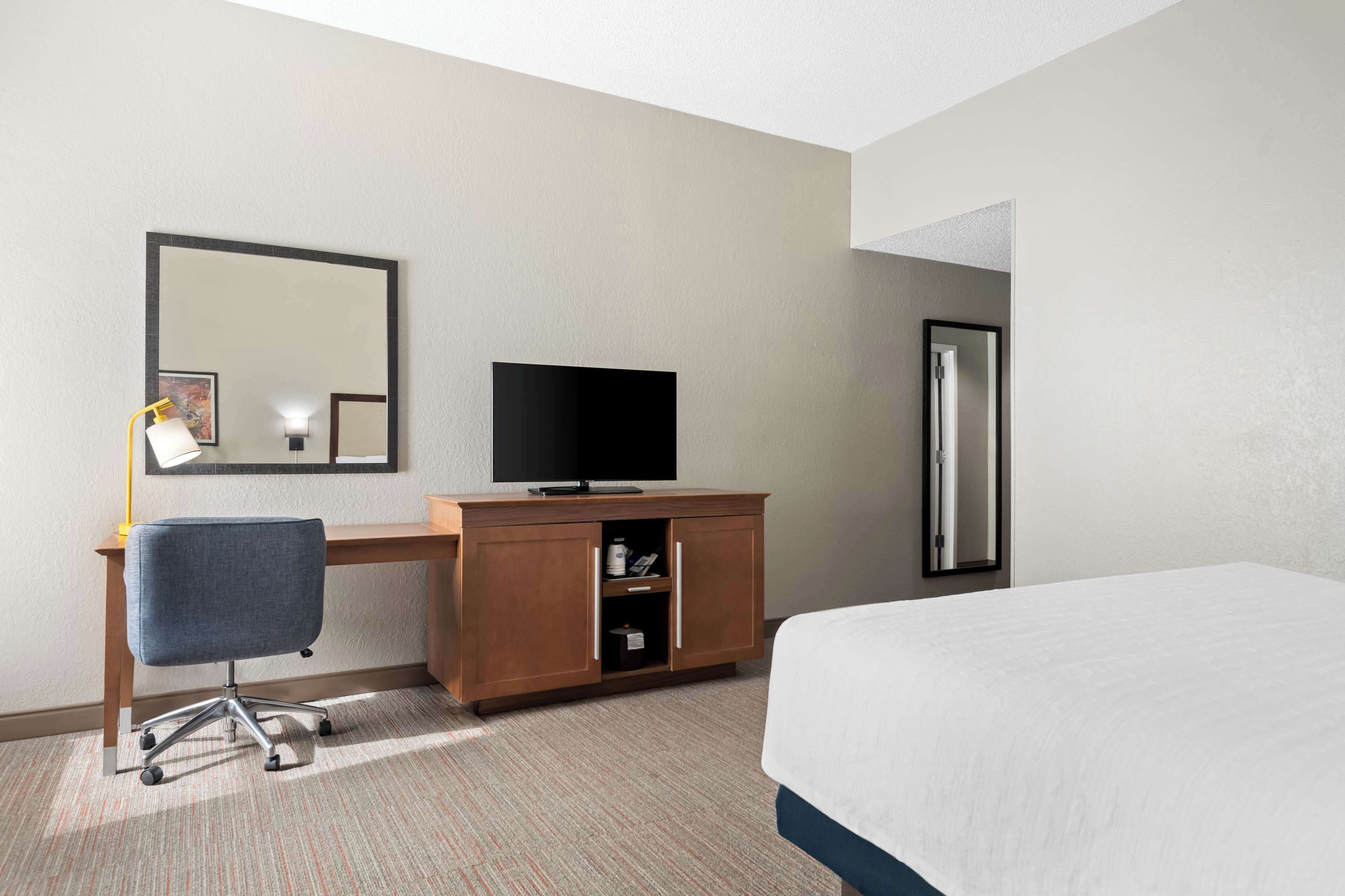 A hotel room with a bed, a desk with a television, a chair, and a wardrobe.