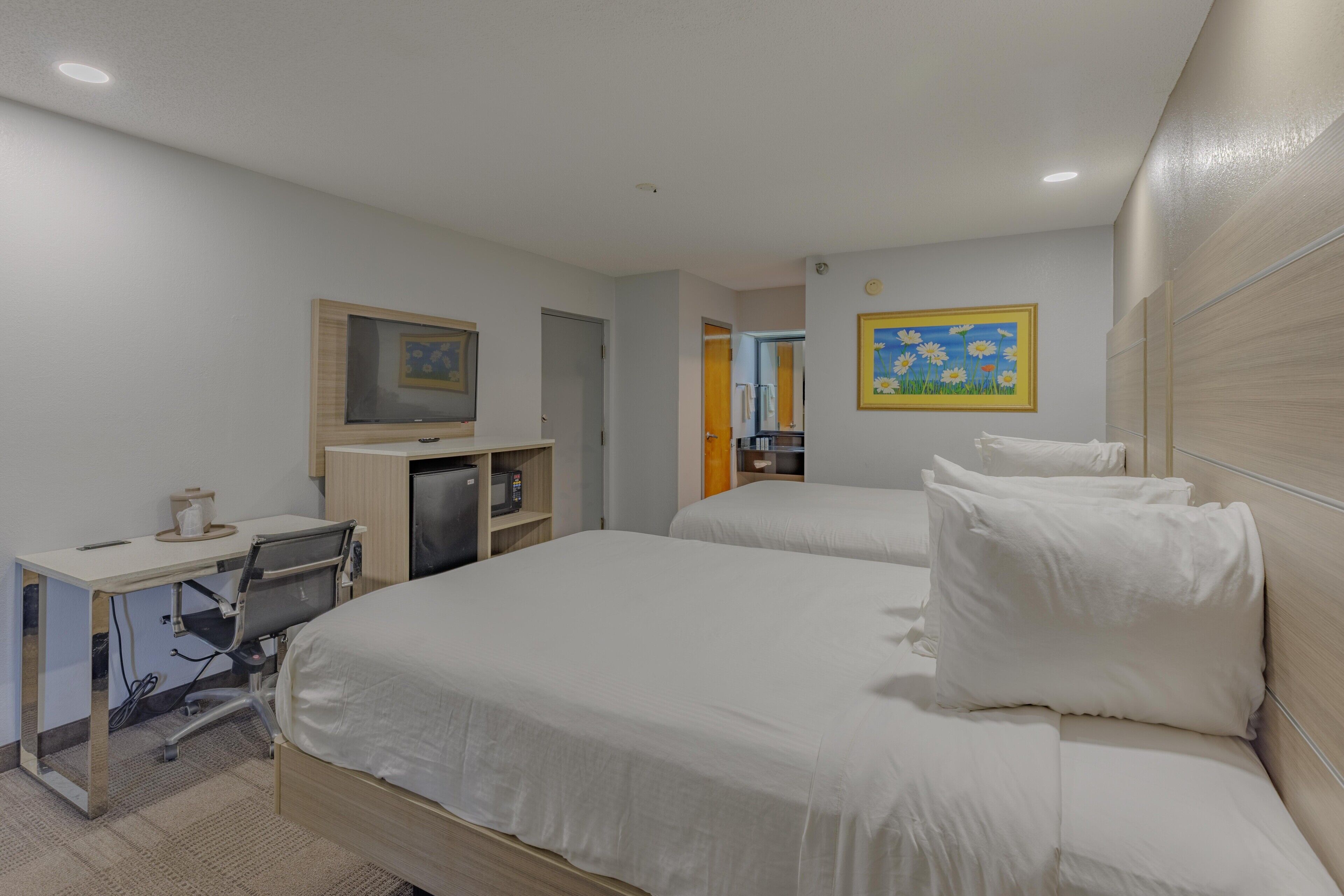A hotel room with two beds, a desk, a chair, a microwave, and a small kitchenette.