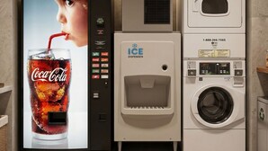 Un distributeur automatique orné d’une publicité pour Coca-Cola, muni d’un point d’eau et d’une machine à laver.