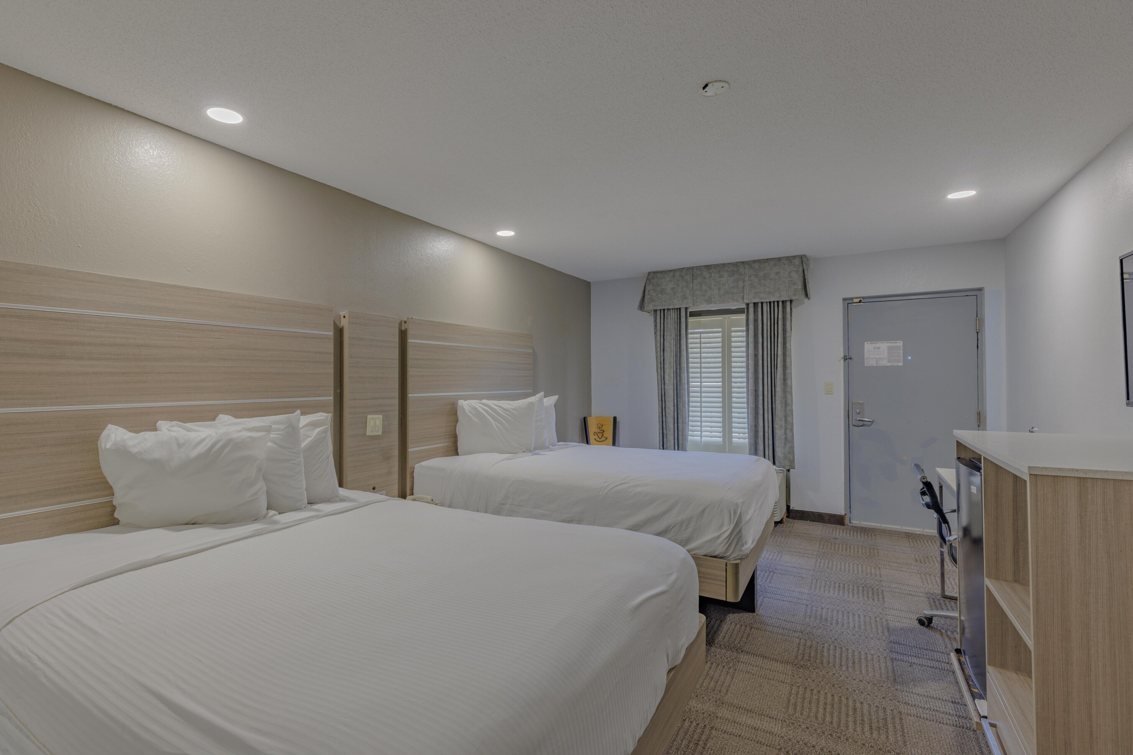 A hotel room with two beds, a desk, and a door.