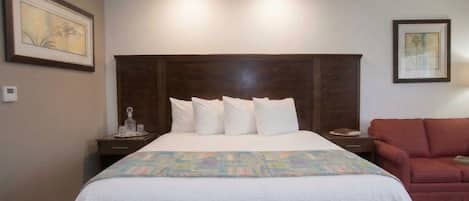 A hotel room with a large bed, a wooden headboard, a red sofa, and two framed pictures on the walls.