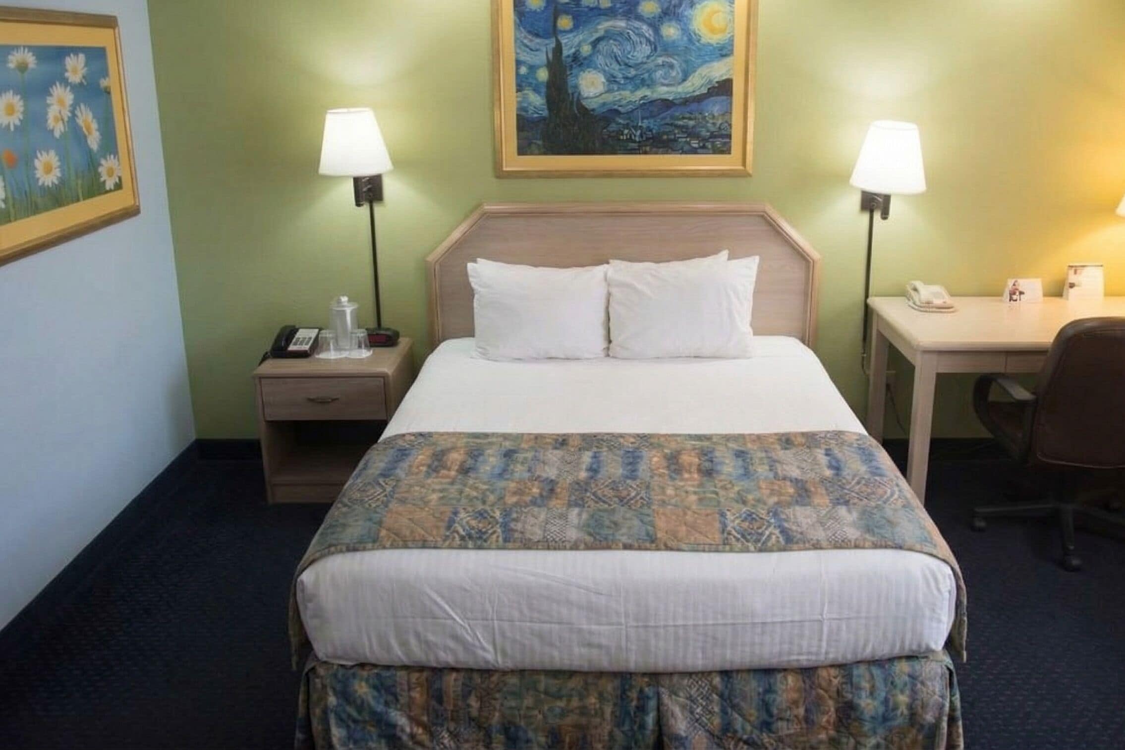 Ein Hotelzimmer mit einem Bett, zwei Nachttischlampen, einem Schreibtisch, einem Stuhl, einem Nachttisch und einem Bild an der Wand.