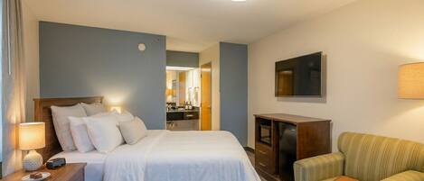 Une chambre d’hôtel avec un lit, un bureau doté d’une lampe, une télévision, une chaise, et une salle de bain visible au fond.