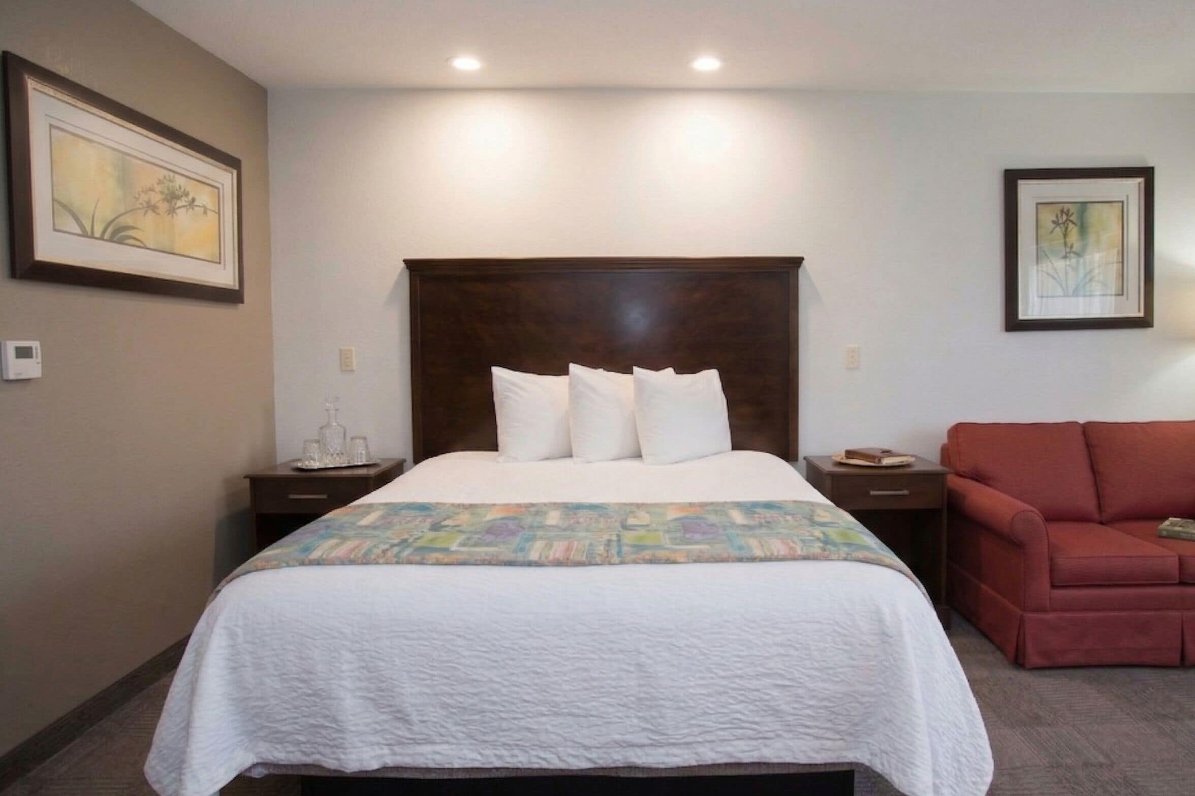 Quarto de hotel com uma cama grande, um sofá vermelho e duas mesas de cabeceira.