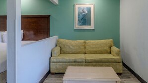 Une pièce avec un lit, un canapé vert, un tableau encadré au mur et une petite table.
