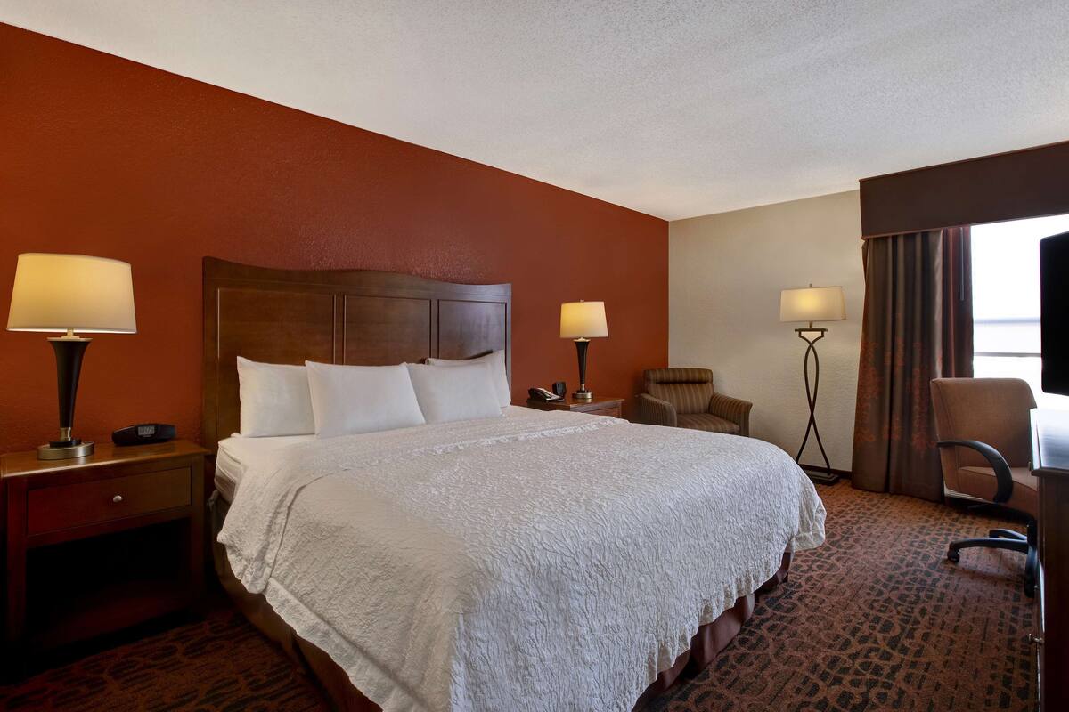 A hotel room with a large bed, two bedside tables with lamps, a chair, and a desk.