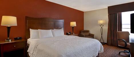 A hotel room with a large bed, two bedside tables with lamps, a chair, and a desk.