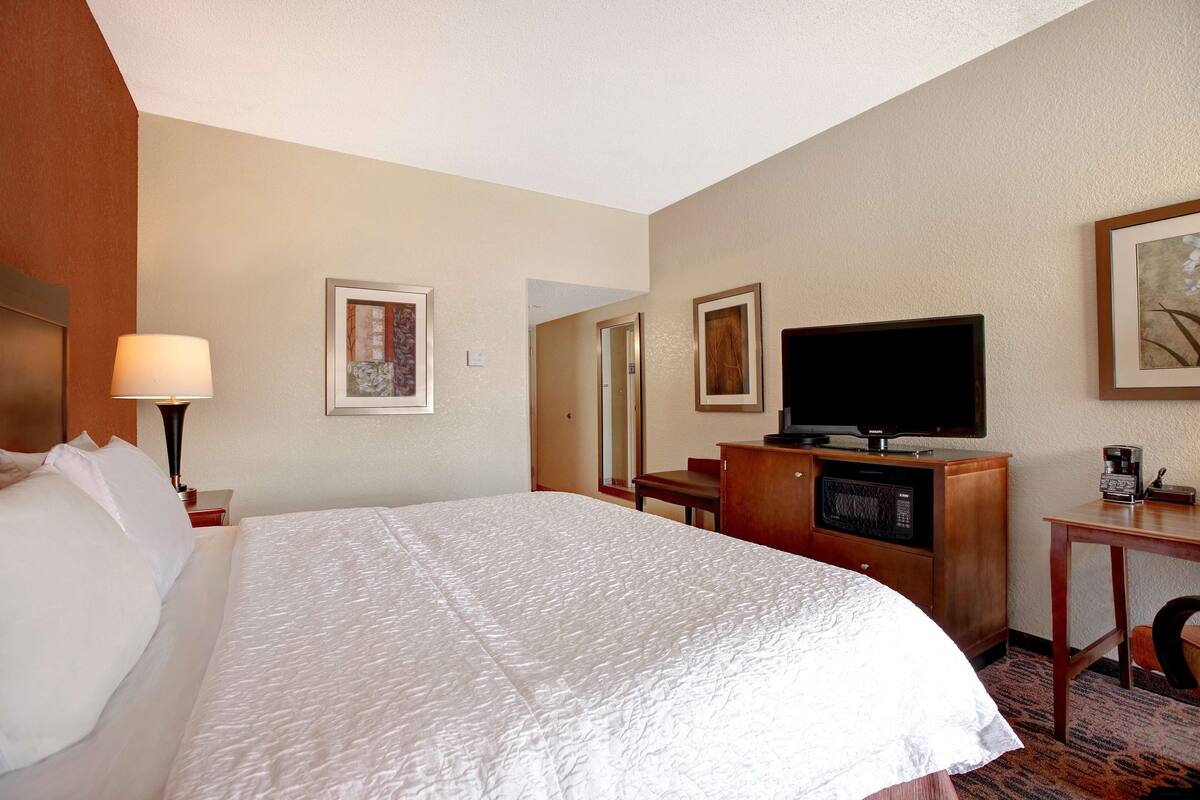 A hotel room with a large bed, a television, a desk with a microwave, and a coffee maker.