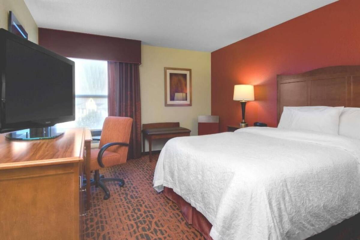 A hotel room with a bed, desk, chair, television, and a window with curtains.