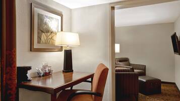 Habitación de hotel con un escritorio de madera, una silla, una lámpara, un cuadro en la pared, un sofá y una alfombra estampada.