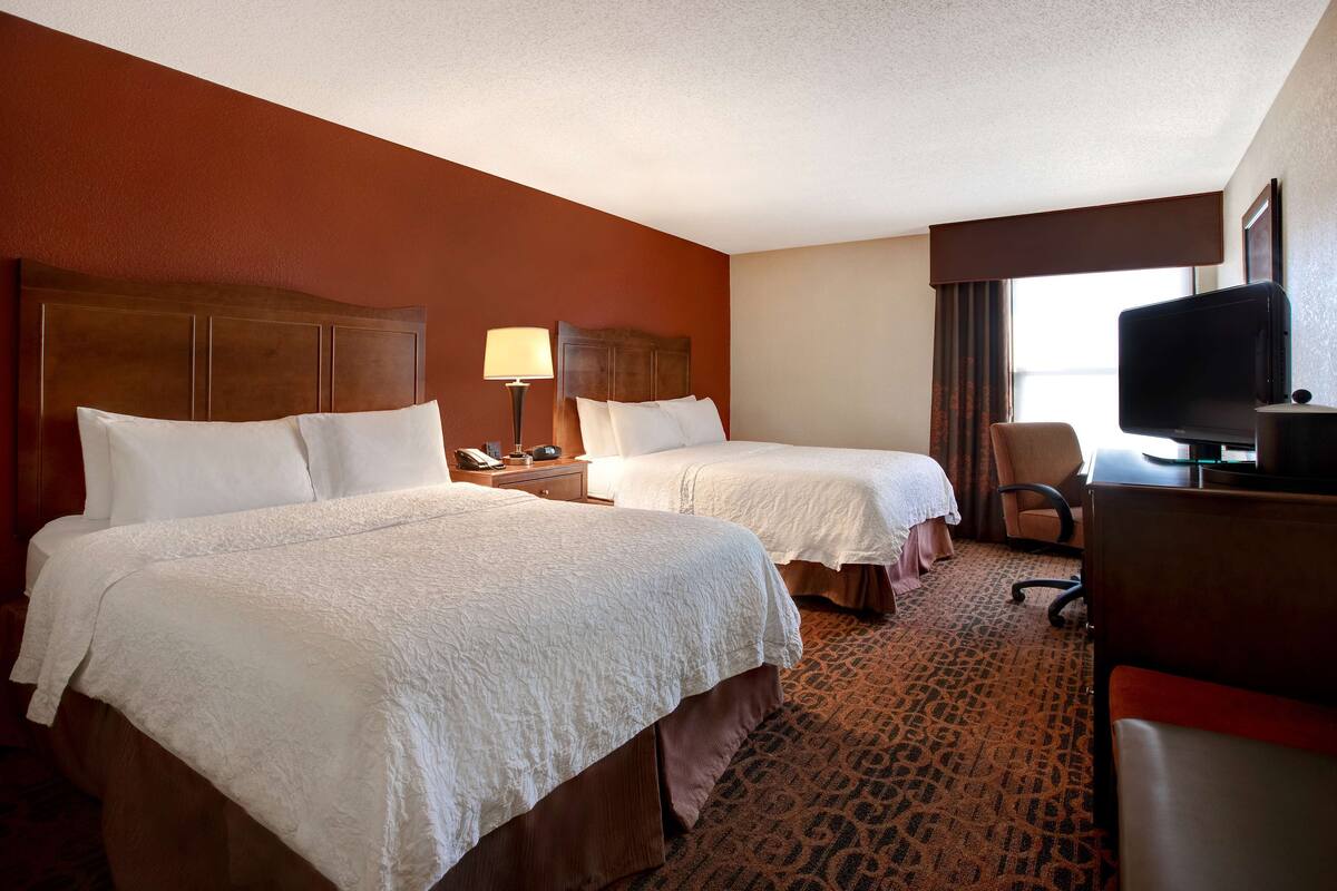A hotel room with two beds, a desk with a television, and a patterned carpet.