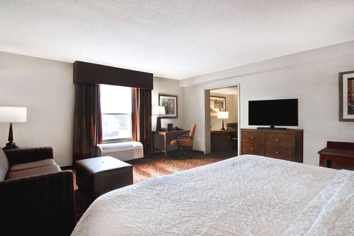 A hotel room with a large bed, a desk, a chair, a television, and a window with curtains.