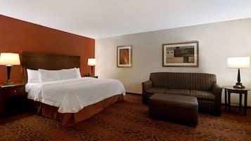 A hotel room with a large bed, a sofa, a small table, and two lamps.