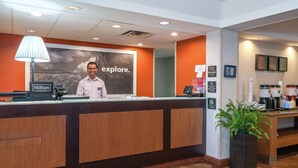 Un mostrador de recepción de hotel con un cartel grande que dice 'explore', una pantalla digital y un letrero de 'Hilton Honors'.