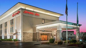 Un hotel Hampton Inn con fachada moderna, un acceso cubierto y un asta de bandera.