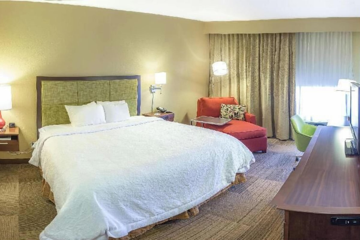 A hotel room with a large bed, a desk, a chair, and a television.