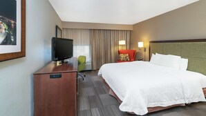 Una habitación de hotel con una cama, un escritorio con televisor, una silla y una lámpara.