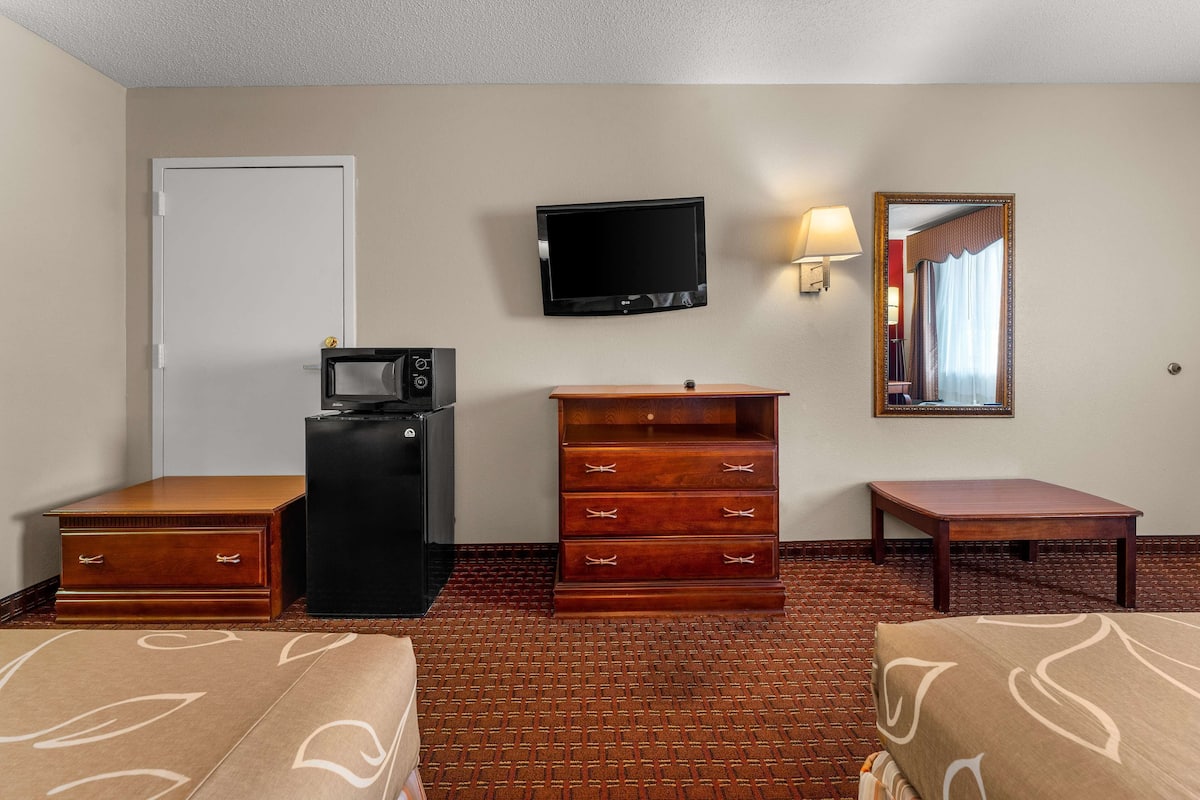 A hotel room with a bed, a dresser, a desk, a television, and a mirror.