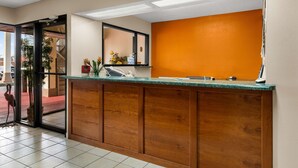 A reception area with a wooden counter, a large mirror, and a view of the outside through a glass door. - Americas Best Value Inn Montezuma (Montezuma)